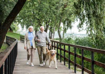 senior husband and wife walking dog on a boardwalk